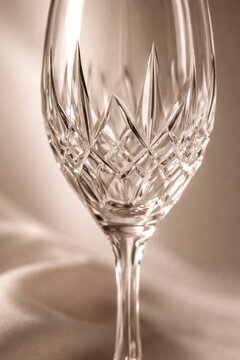 Crystal wine glass with intricate cut patterns reflecting light, placed on a soft surface, showcasing elegance and fine craftsmanship in a blurred background.