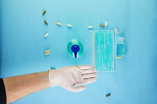 The concept of coronavirus COVID-19, How to protect yourself from infection. Hand in protective glove and disinfectant gel, mask and pills. Flat lay on a blue background.