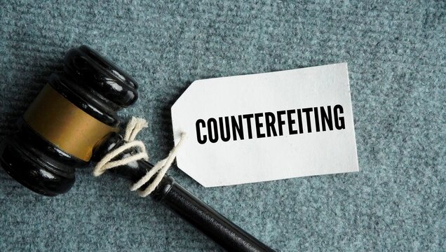 Judge gavel with the words Counterfeiting is the illegal creation, reproduction, or imitation of genuine items such as currency, consumer goods, documents, or brand trademarks with the intent to decei