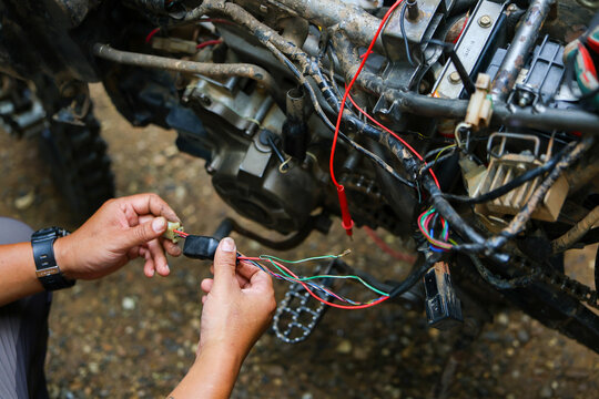 Mechanic repair motorcycle engine wiring outdoors with exposed electrical cable and tools