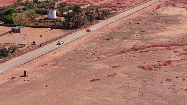 Aerial view of surroundings from El Cotillo, a coastal town located on the island of Fuerteventura, Canary Islands, Spain. Drone POV of windmill and car passing on the dirt road,