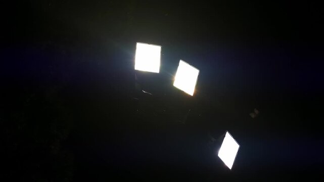Static shot footage shows insects and bats flying near the bright light of powerful stadium lights. Low angle video.