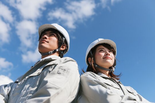 建設現場の若い男女が未来を見据え青空を仰ぐ