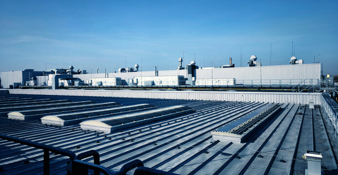 Industrial rooftop with corrugated metal panels, rows of vents and chimneys
