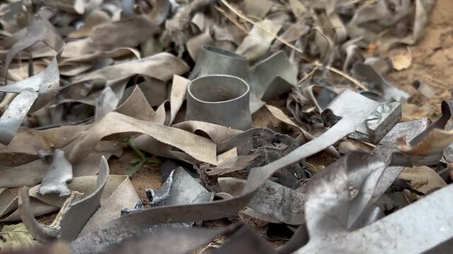 Pile of collected remains from detonated KOBE 3B30 dual-purpose cluster submunitions: torn metal casings, fragments and faded fabric stabilizer ribbons heaped on sandy ground