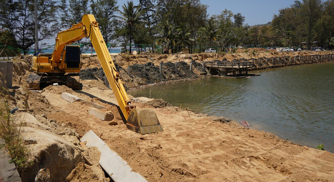 Building process city levee. Excavator dredging pond bank