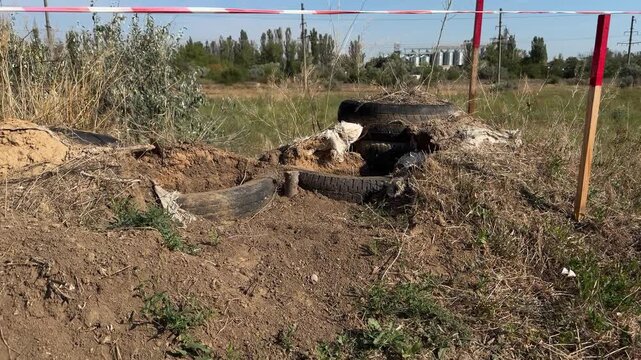 Cordoned-off position with red and white warning tape, wooden pickets and an earth mound reinforced with old tyres on a site where dangerous objects are searched for and disposed of.