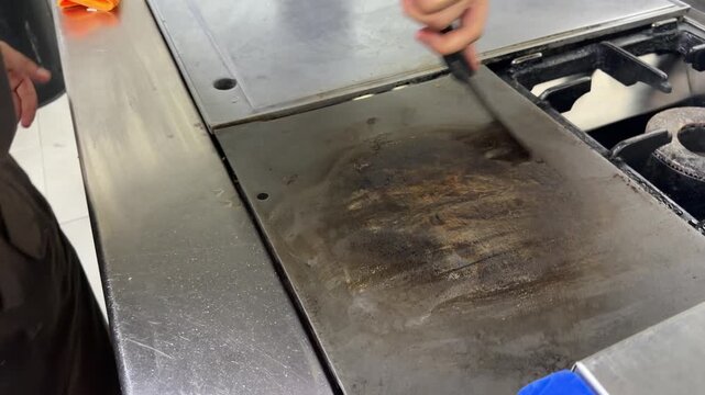 Professional chef cleaning a dirty griddle with a scraper