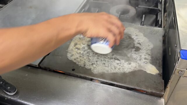 Restaurant worker cleaning a commercial kitchen griddle