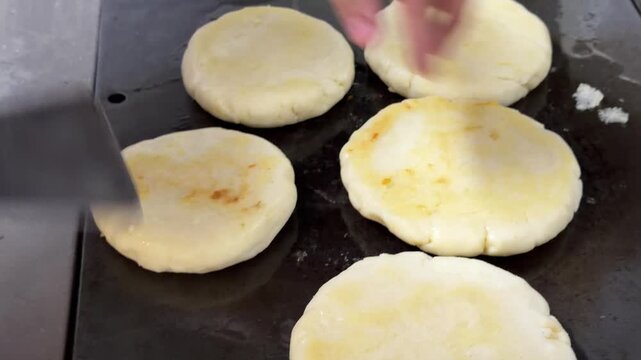 Chef cooking arepas on a hot griddle in a restaurant kitchen