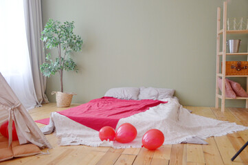 Interior of a children's or youth room with a mattress on the floor, a red bedspread and balloons © Елена Пантюхина