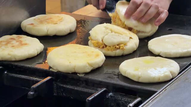 Chef cooking stuffed arepas on a griddle in a restaurant kitchen