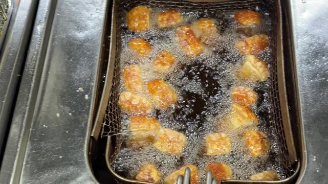 Crispy pork belly pieces frying in deep fryer basket