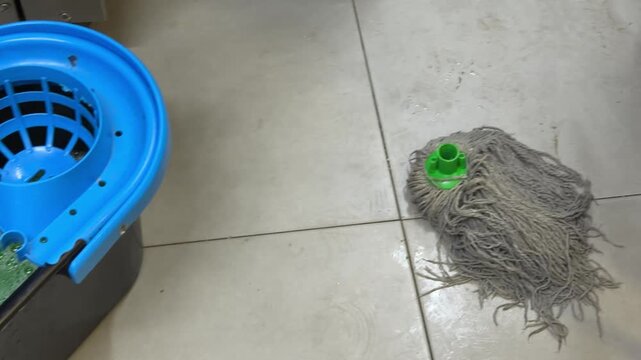 Person mopping a tiled floor with a bucket and wringer