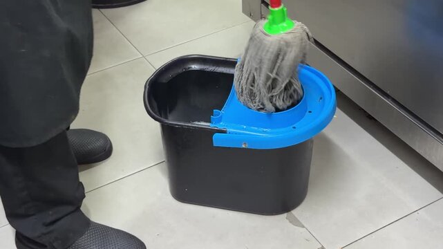 Restaurant worker wringing out a mop in a bucket