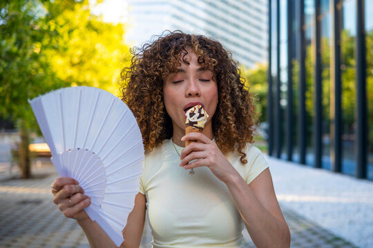 Woman enjoying ice cream and fan cooling down in summer heat