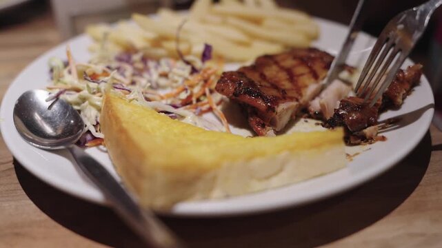 Grilled chicken steak served on a white plate with crispy french fries, fresh coleslaw salad, and thick buttered toast. Close-up restaurant meal on a wooden table with soft bokeh background.