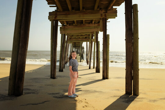 Young woman standing under a wooden pier on the beach