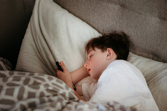 Young boy scrolling on his phone in bed