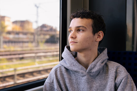 Young man in hoodie looks out a train window