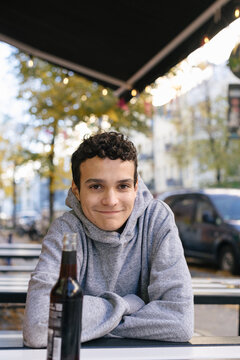 A young man sits smiling at an outdoor cafe table