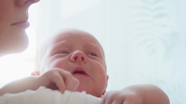 Close up shows mother talking to crying infant on shoulder, using calm voice, facial attention, and close contact to offer reassurance, comfort, and emotional support at home indoors.