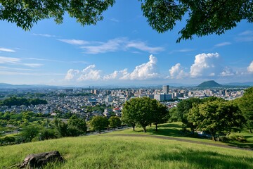 Obraz premium 青空と白い雲広がる緑豊かな丘から見下ろす日中の街並みパノラマ風景