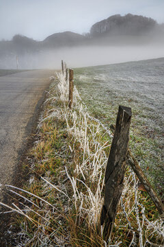 Winter landscape with frost-covered grass, a wooden fence and misty hills in the background, Hauenstein, Solothurn, Switzerland