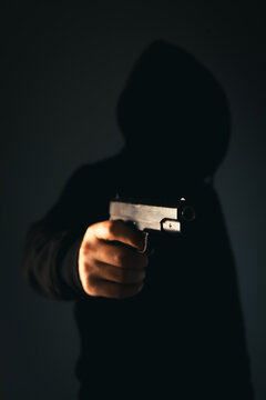 View of a Criminal holding a gun in front of a dark background