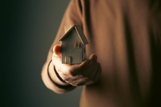 Man holding a model of a house in his hands on a dark background
