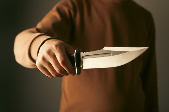 Man holding knife on dark background, closeup view. Criminal concept