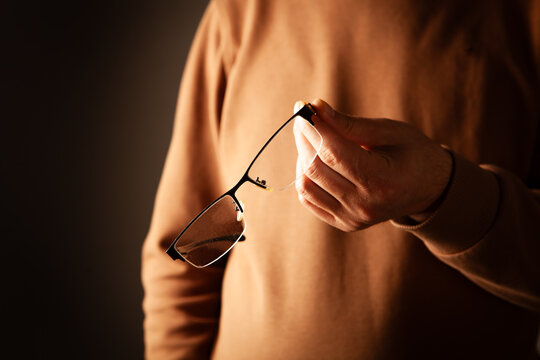 Close-up of man's hands holding eyeglasses on dark background