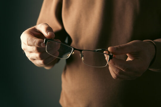 Close-up of man's hands holding eyeglasses on dark background