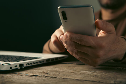Man using mobile phone and laptop at wooden table. Close up.