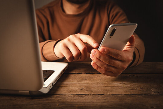 Man using mobile phone and laptop at wooden table. Close up.