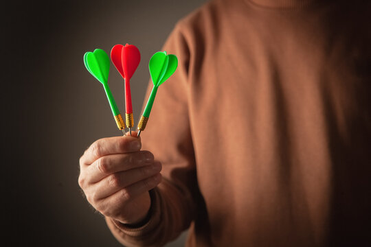Red and green darts in a man's hand on a dark background