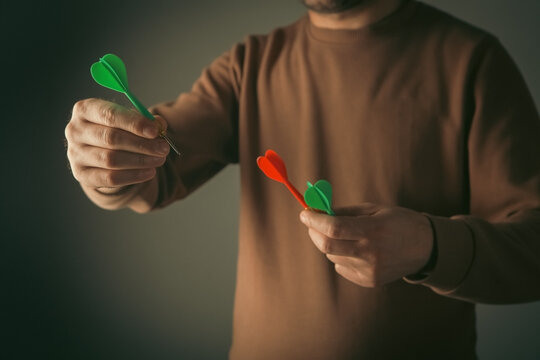 Red and green darts in a man's hand on a dark background