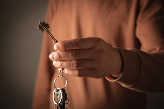 Close up of male hand holding keys on dark background with copy space