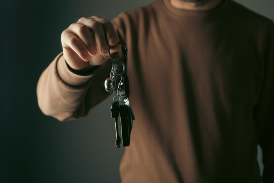 Close up of male hand holding keys on dark background with copy space