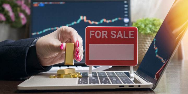 Liquidating physical assets. Hand selling gold bullion online against a background of stock market charts.