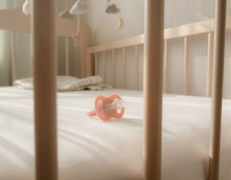 A pink baby pacifier rests on a white sheet inside a nursery crib. Soft morning sun illuminates the newborn bedroom decor, creating a calm lifestyle mood and peaceful atmosphere for a toddler's nap, c