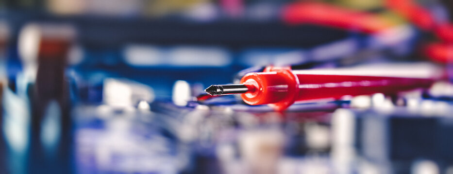 Computer repair and electronics maintenance concept. Macro close-up of a red multimeter probe resting on a blue circuit board.