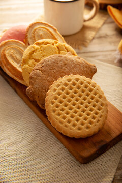 Traditional Mexican sweet bread variety on a rustic wooden board. Variety of authentic pan dulce including puerquito, orejas, and cookies over a neutral tablecloth background for bakery concept.