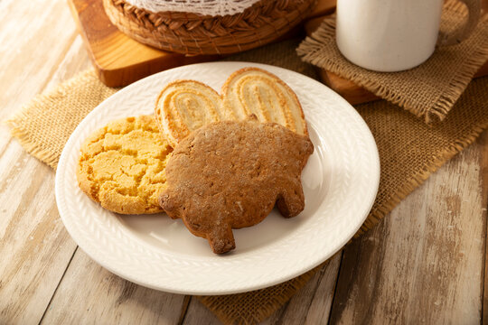 Traditional Mexican sweet bread variety on a rustic wooden board. Variety of authentic pan dulce including puerquito, orejas, and cookies over a neutral tablecloth background for bakery concept.