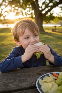 Happy child enjoying a sandwich at a picnic table in nature