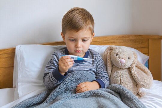 Sick child checking temperature with digital thermometer in bed