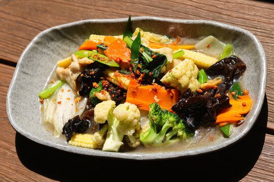 Stir-fried mixed vegetables capcay with broccoli, cauliflower, carrots, wood ear mushrooms, baby corn, bok choy, and fried garlic served in a gray ceramic bowl.