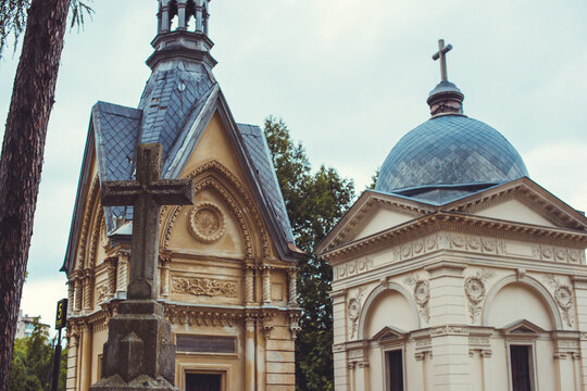 Ancient cemetery monuments featuring ornate gravestones, weathered stone sculptures and historic tombs surrounded by trees. Atmospheric old-world funerary architecture and timeless memorial details 
