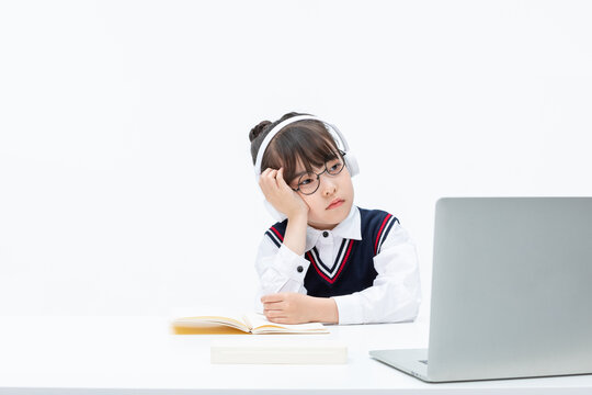 Bored schoolgirl studying online with laptop headphones and book