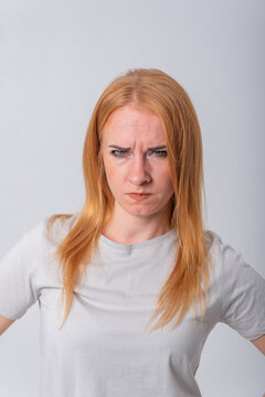 Young redhead woman glaring with anger and frustration, scowling in displeasure and irritation while staring ahead, conveying upset, stress and negative emotion on white background